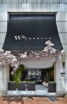 an entrance to a building with cherry blossoms on the outside and in front, there is a black awning that says m & s