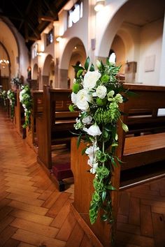 flowers are placed on the pews in this church wedding ceremony aisle arrangement, which is decorated with greenery and white roses