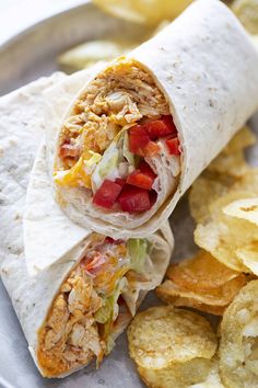 a chicken wrap with lettuce, tomato and cheese on it next to chips