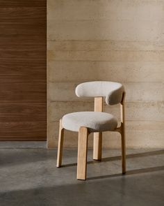 a white chair sitting in front of a wall with a wooden frame on it's back