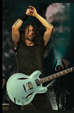 a man with long hair is holding his guitar in front of him and the other hand on his head