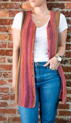 a woman standing in front of a brick wall wearing a multicolored knitted vest