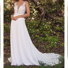 a woman in a white wedding dress posing for the camera with trees and bushes behind her