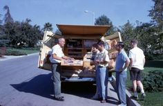 several people standing in the back of a moving truck with boxes on it's flatbed