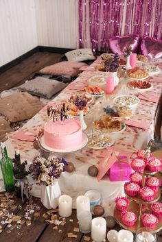 a table filled with cakes and cupcakes on top of wooden tables covered in pink decorations