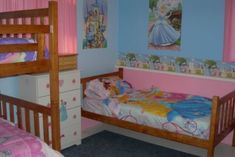 two children's beds in a pink and blue bedroom with princess pictures on the walls