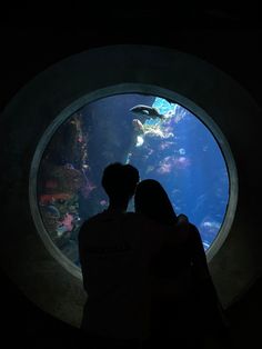 two people standing in front of an aquarium looking at the fish