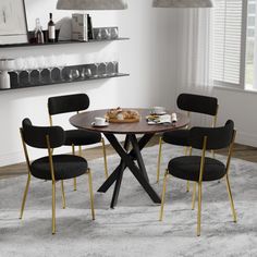 a round table with four black chairs around it in a white living room, next to an open book shelf