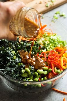 someone pouring dressing into a bowl filled with vegetables and carrots to make a salad