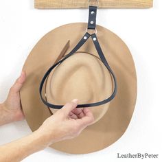 a person is holding a hat on a wall with a leather strap attached to it