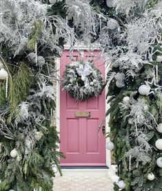 a pink door surrounded by christmas decorations and greenery in front of a red door