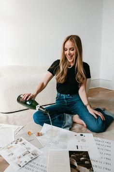 a woman sitting on the floor pouring wine into a glass with papers scattered around her