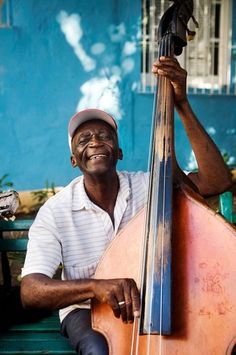 a man sitting on a bench with a large instrument in his hand and smiling at the camera