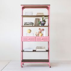 a pink bookcase with drawers and books on the top shelf, against a white wall