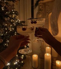 two people are toasting with wine glasses in front of a christmas tree and lit candles