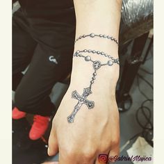 a person with a rosary tattoo on their arm and wrist, holding a cross in one hand