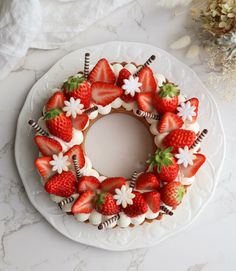 a white plate topped with a cake covered in strawberries and cream frosting on top of a marble counter