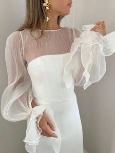 a woman wearing a white dress with sheer sleeves