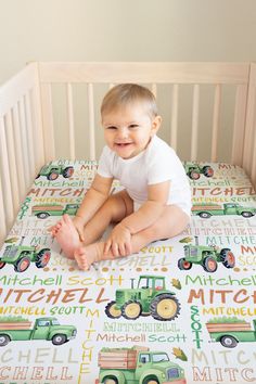 a baby sitting on top of a bed next to a crib with a green tractor