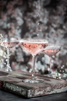 two wine glasses filled with pink liquid sitting on top of a wooden table next to each other