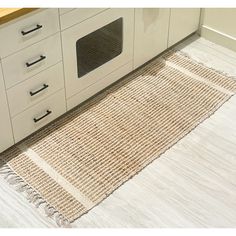 a kitchen area with white cabinets and beige rugs on the floor next to an oven