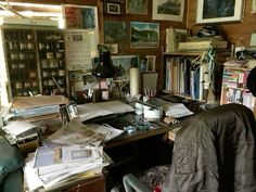 a cluttered desk with lots of books and pictures on the wall in front of it