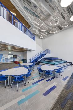 an empty room with tables and chairs in the foreground, blue railings to the second floor