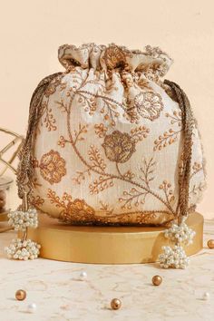 "Colour: Cream Embroidered front and back. Dimensions (LxB): 9.5\" x 9\" (24 cm x 23 cm) Handle drop: 5\" (13 cm) Material : Embroidered poly silk, poly satin lining, woven golden thread drawstrings and handle, scallop lace and pearl tassels." Gift Embroidered Beige Potli Bag, Festive Gold Embroidered Potli Bag, Beige Rectangular Potli Bag For Festivals, Festive Beige Pouch Shoulder Bag, Beige Embroidered Fabric For Festive Occasions, Festive Embroidered Beige Potli Bag, Traditional Gold Embroidery Potli Bag, Gold Embroidered Pouch As Gift, Gold Embroidered Pouch For Gift