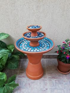 three tiered ceramic fountain with blue and white tiles on it next to potted plants