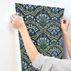 two hands holding up a piece of fabric with floral designs on it, against a white wall