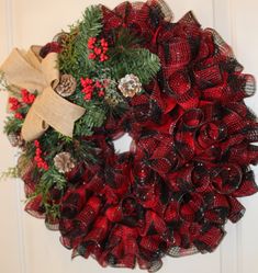 a red and black wreath hanging on the front door with pine cones, evergreens and berries