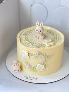 a yellow cake decorated with an animal figurine and flowers on it's side