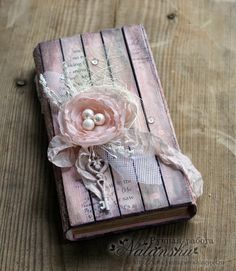 an old book with a flower and pearls on the front is sitting on a wooden table