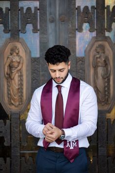 a man wearing a purple vest and tie standing in front of an ornate wall with carvings on it