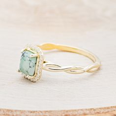 a gold ring with a green stone surrounded by white and yellow diamonds on a beige background