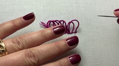 a woman's hand with red nail polish and gold ring next to some thread