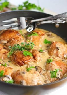 a skillet filled with chicken and mushrooms covered in gravy, garnished with parsley