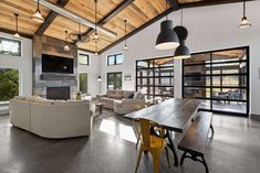 a large open living room and dining area with wooden ceiling beams, white couches, yellow chairs, and a fireplace