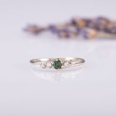 a close up of a ring on a table with flowers in the background and a purple flower behind it