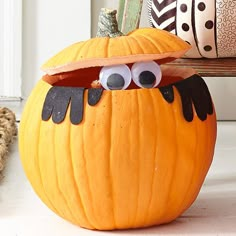 a pumpkin with googly eyes on it sitting next to a stuffed animal and other items