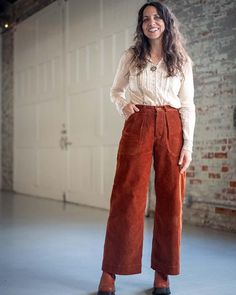 a woman standing in front of a garage door wearing brown pants and a white shirt