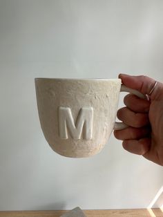 a hand holding a coffee cup with the letter m on it