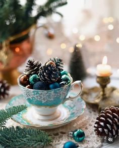 a tea cup filled with blue balls and pine cones on top of a saucer