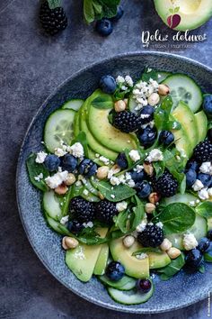 a blue bowl filled with cucumber, blackberries and spinach on top of a table