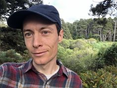 a man wearing a hat standing in front of some trees