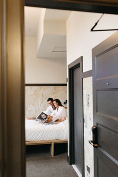 two people are sitting on a bed looking at a laptop computer in the doorway to their bedroom