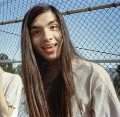 a man with long hair standing in front of a fence and holding a cell phone