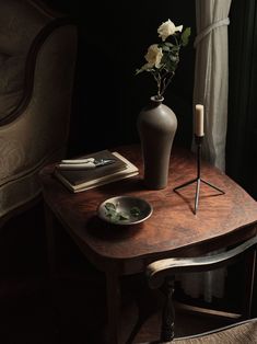 a table with a vase, candle and some books on it next to a window