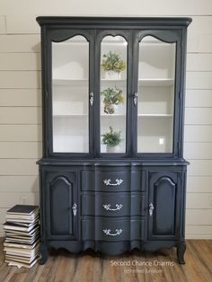 an old china cabinet painted black with white trim and glass doors, sitting on top of a hard wood floor