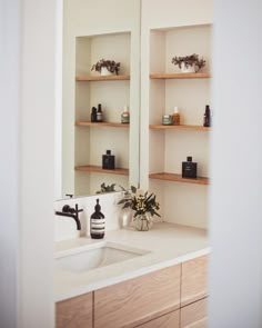 a bathroom sink sitting under a mirror next to a shelf filled with bottles and vases